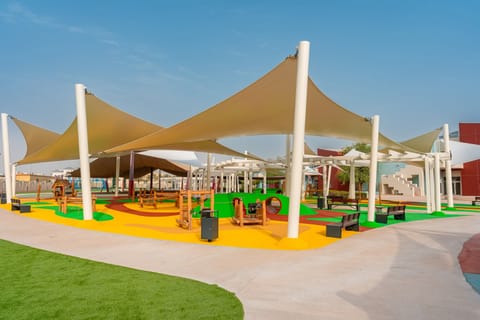 Sand-coloured shade sails over a playground with green and yellow safety flooring