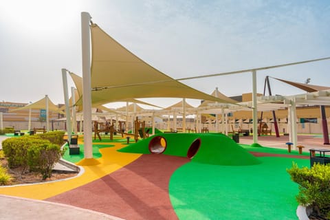 Tall-mast shade sails over a play area with mounds and tunnels