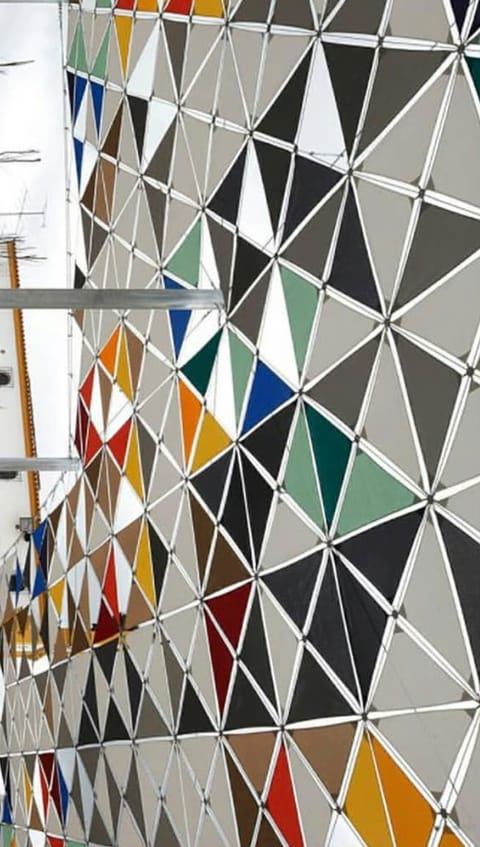 Coloured triangular membrane panels on a curving steel frame