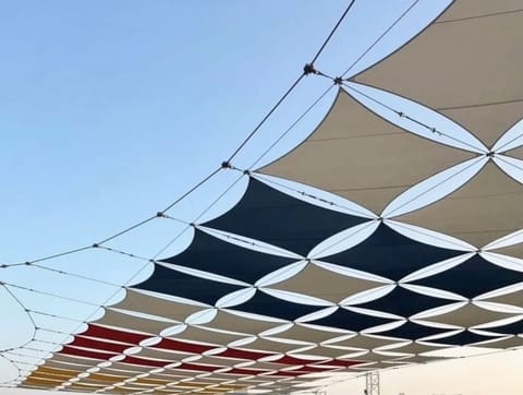 Grid of charcoal, sand and red shade sails seen from below
