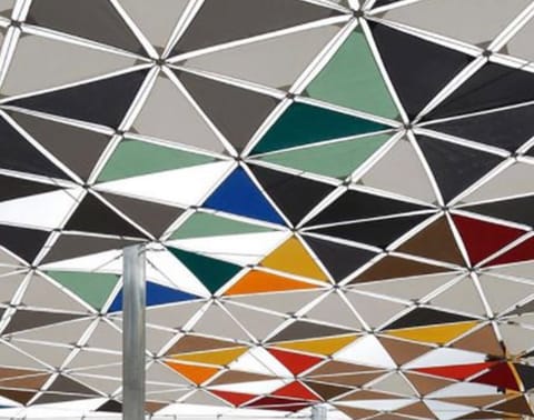 Canopy of coloured triangular membrane panels on a steel grid, from below