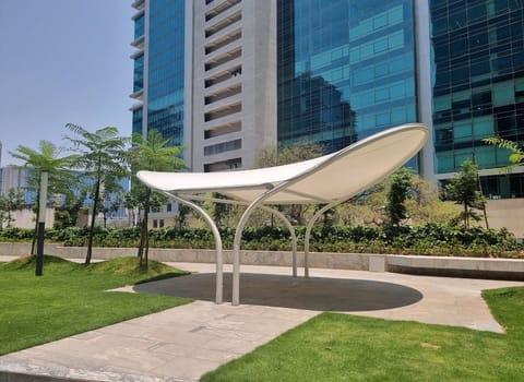 Saddle-shaped white tensile shade over a paved seating circle between towers
