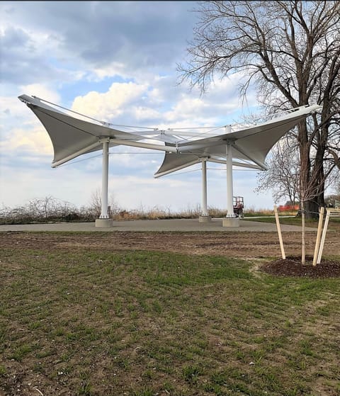 Pair of winged white tensile canopies on steel columns in a park
