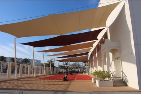 Overlapping sand and brown shade sails running along a building and court